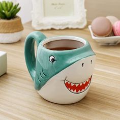 a coffee mug with a shark face painted on the side and eggs in bowls behind it