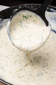 a ladle full of white sauce being poured into a skillet