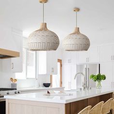 two wicker lamps hanging from the ceiling in a kitchen with white cabinets and counter tops