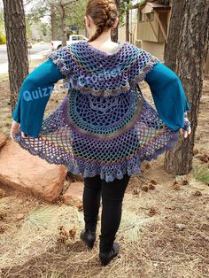 a woman is standing in the woods with her back to the camera, wearing a crocheted dress