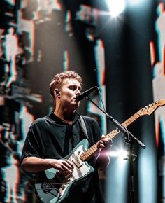 a man holding a guitar while standing in front of a microphone on top of a stage