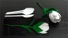 three plastic spoons and two white flowers with green stems on a black table top