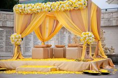 an outdoor ceremony with yellow and white flowers on the stage, draped in gold draping