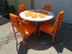 an orange and white dining table with four chairs on the side walk in front of a garage door