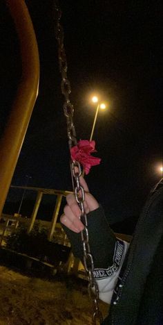 a person holding onto a chain with a red flower on it's end, at night