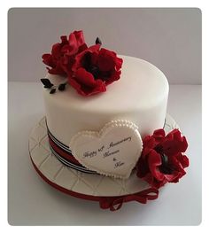 a white cake with red flowers on top and a heart shaped plaque in the middle