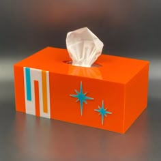 an orange tissue box with blue stars on the side and a white tissue in it