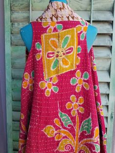 the back of a pink and yellow jacket hanging on a wooden wall with shutters