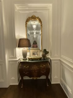 a room with a table, mirror and lamp on it in front of a white wall