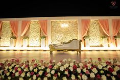 a white couch sitting in front of a stage with flowers on the floor and curtains behind it