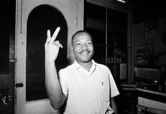 a black and white photo of a man making the peace sign in front of a door