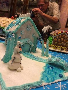 a man taking a photo of a frozen world cake with snowman and ice house