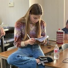 a woman sitting on top of a chair in front of a desk with another person behind her