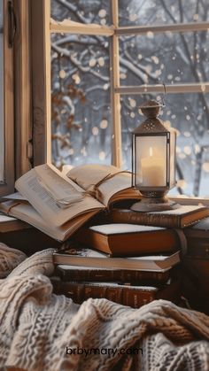 an open book sitting on top of a pile of books next to a candle and window