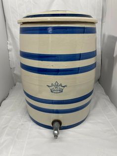 a large blue and white striped container on a white surface with a metal hook in the middle