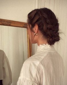 a woman standing in front of a mirror looking at herself in the mirror with her hair pulled back