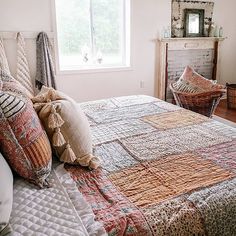 a bed with many pillows and blankets on it in a bedroom next to a window