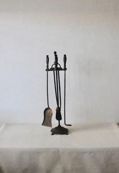 an iron hook and two candles on a white tablecloth with a wall in the background