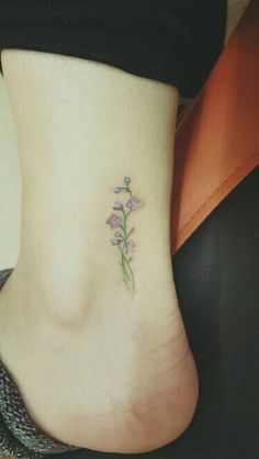 a small flower tattoo on the side of a woman's foot, with purple flowers