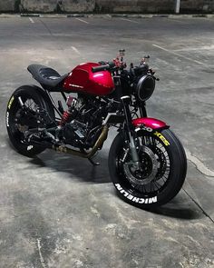 a red and black motorcycle parked on top of a cement parking lot next to a building