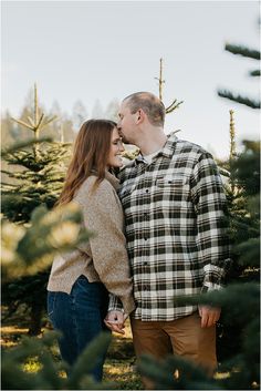 a man and woman standing next to each other in front of pine trees at sunset