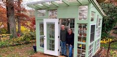 two people standing in the doorway of a small green shed with windows on each side