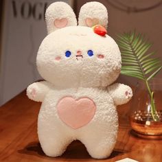 a white stuffed animal sitting on top of a wooden table next to a vase filled with flowers