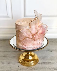 a pink and gold cake on a glass plate with a golden stand next to it