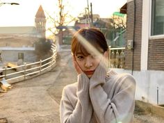 a woman standing in front of a building with her hands on her head and looking at the camera