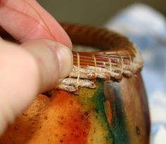 a person is holding a piece of food in front of a pot that has been painted with different colors