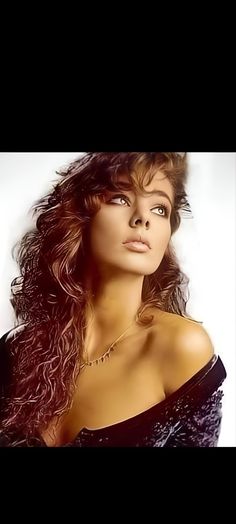 a woman with long curly hair wearing a black dress and posing in front of a white background