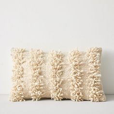 a white pillow with fringes on the front and back of it, against a white wall