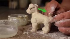 a person is making a small dog out of clay with green arrow pointing to it