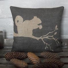 a pillow with a squirrel on it next to pine cones