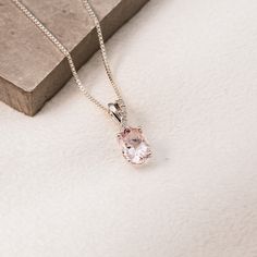 a necklace with a pink stone hanging from it's side on a white surface