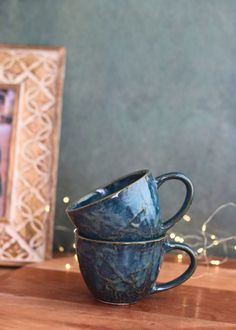 two blue coffee cups sitting on top of a wooden table next to a framed photo