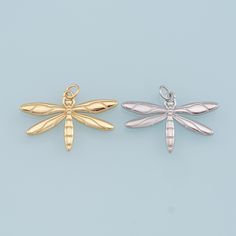 two dragonfly charms sitting side by side on a light blue background, one in gold and the other in silver