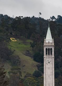 a tall clock tower sitting on top of a lush green hillside covered in trees and bushes