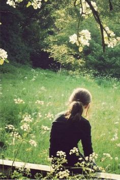 black and white photograph of woman sitting on bench in field with wildflowers behind her