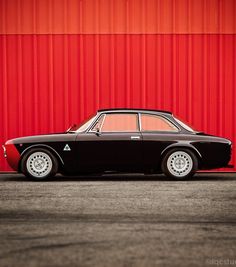 an old black car parked in front of a red wall