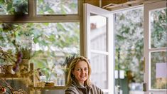 a woman sitting at a table in front of a window with potted plants on it