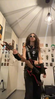 a woman with long hair and sunglasses playing an electric guitar in a room full of pictures