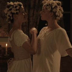 two women standing next to each other with flowers in their hair and one wearing a white dress