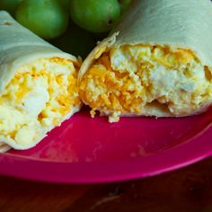 an egg burrito on a pink plate with grapes