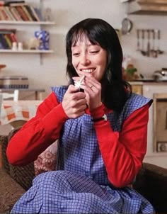 a woman sitting on top of a couch holding a cell phone in her hand and laughing