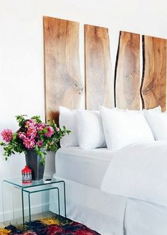 a bed with white sheets and pillows next to a flower vase on a small table