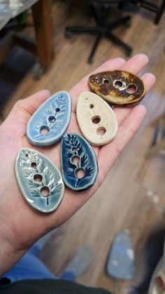 a person is holding five different buttons in their hand, each with leaves on them