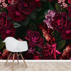 a white chair sitting in front of a wall with red flowers and leaves on it