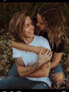 a man and woman sitting on the ground hugging each other with their arms around each other