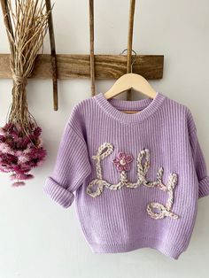 a purple sweater hanging on a wooden hanger next to dried flowers and twigs in the background